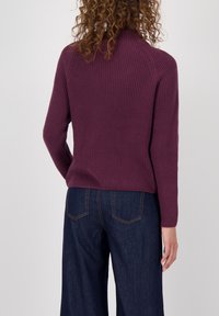 Geribbelde paarse trui met hoge nek en lange mouwen, gecombineerd met een paar wijde denim broeken. De achterkant heeft een eenvoudig ontwerp.