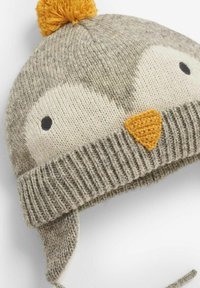 Grå stickad mössa med ett pingvinansikte som design. Har runda ögon, en triangulär orange näbb och en gul pom-pom på toppen. Öronlappar.