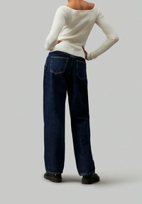 Witte geribde longsleeve top gecombineerd met loszittende donkerblauwe denim jeans. De jeans hebben twee achterzakken en een recht gesneden pijpdesign.