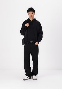 Sweatshirt preto com um bolso frontal e cordões, combinado com jeans largos pretos e ténis brancos com realces pretos.