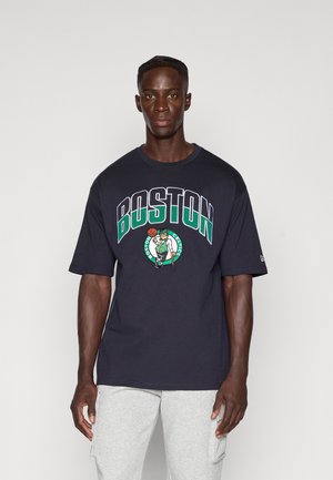 Tamno plava oversized majica ima natpis "BOSTON" u hrabrom bijelom i zelenom pismu, s grafikom leprechauna koji drži košarkašku loptu.