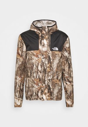 Veste à capuche North Face avec motif camouflage arbre marron et beige, panneaux d’épaule noirs, boutons sur le devant et logo sur la poitrine.