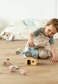 Heled puitkuiroja helesinise kerega ja hallide ratastega, virnastatud kollase kaare peale, ümbritsetud väikeste loomafiguuride ja pilvekujuga plokiga.