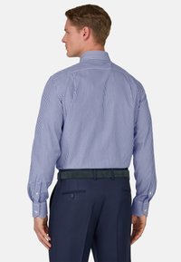 Camisa de vestir a rayas en azul y blanco, con un cuello clásico, mangas largas y puños abotonados, combinada con pantalones azul marino y un cinturón verde.