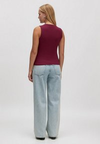 Burgunderfarbener, gerippter Tanktop ohne Ärmel; kombiniert mit hellblauen, weiten Jeans mit Gesäßtaschen. Glatte Textur und taillierte Form.