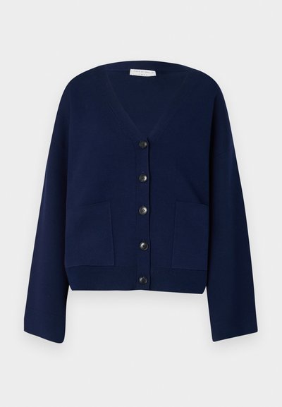 Marineblå strikket cardigan med V-hals, seks sorte knapper og to frontlommer. Har overdimensjonerte ermer og cropped nederkant.