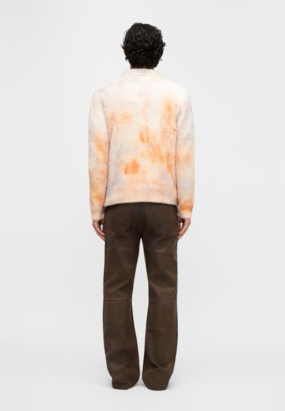 Γούνινο σακάκι σε παστέλ αποχρώσεις με μαλακή υφή, που διαθέτει πορτοκαλί και ροδάκινι κηλίδες· συνδυάζεται με καφέ παντελόνι φαρδιάς γραμμής.