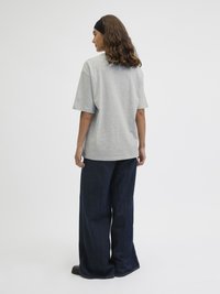 Šedé bavlněné tričko s volným střihem a krátkými rukávy, doplněné širokými tmavě modrými džíny, které představují ležérní outfit.