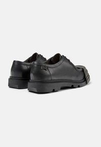 Scarpe in pelle nera con punta tonda, cuciture minime e suola in gomma spessa. Presentano un tacco rinforzato e un logo discreto sul lato.