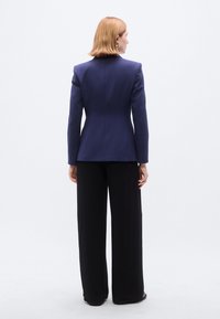 Ναυτικό σακάκι με έντονους ώμους, εφαρμοστή γραμμή και μακριά μανίκια, σε συνδυασμό με μαύρο παντελόνι φαρδιάς γραμμής, με απλό, καθαρό σχέδιο.