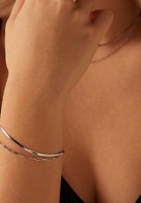 Zilveren armbanden in verschillende texturen en ontwerpen, waaronder een gladde band en een schakelketting, gedragen om een blote pols tegen de huid.
