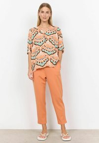 Kortærmet skjorte med orange og teal påfuglefjer mønster; parret med tapered orange bukser og hvide flip-flops.
