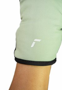 Helle grüne Stoff-Armschlaufe mit schwarzem Besatz. Verfügt über ein weißes Logo im oberen Bereich. Glatte Textur, enger Sitz.