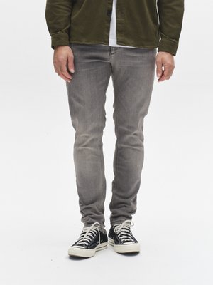 Sive denim hlače s slim krojem, z izpranim učinkom in subtilnim razbarvanjem. Kombinirane s črnimi platnenimi supergami in plastno oblečeno srajco.