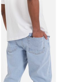 Jeans de mezclilla azul claro con un corte relajado, que cuentan con dos bolsillos traseros y una pequeña etiqueta de la marca visible dentro del bolsillo derecho.