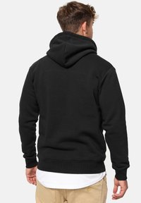 Zwarte hoodie met een ontspannen pasvorm, voorzien van een kangoeroezak en geribde manchetten en zoom. De stof lijkt zacht en comfortabel.
