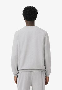 Szürke pulóver hosszú ujjakkal, kerek nyakkivágással, puha textúrával és bordázott mandzsettákkal. Lazán illeszkedő fazon, párosítva hozzá illő nadrággal.