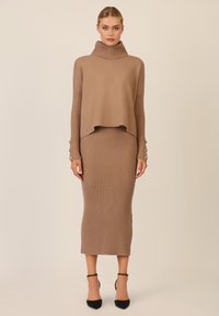 Beige Strickpullover mit hohem Kragen über einem passenden gerippten Midirock; Ärmelakzente mit Knöpfen; strukturierter Stoff überall.