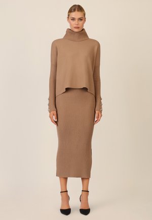 Tan knit sweater with a high collar over a matching ribbed midi skirt; sleeve accents feature buttons; textured fabric throughout.