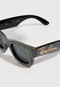 Occhiali da sole neri con montatura testurizzata ricoperta da piccoli borchietti metallici. Caratterizzati da lenti scure e da un logo dorato sul lato.