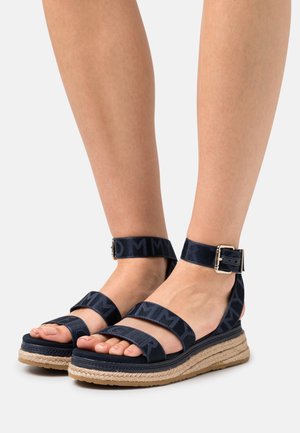 Navy platform sandals with two broad fabric straps and an ankle strap featuring a metal buckle. Jute-trimmed sole, textured black accents.