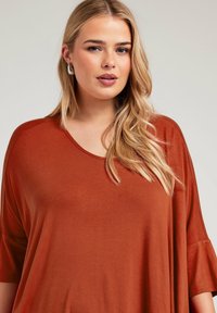 Rostfärgad överdimensionerad topp med rund halsringning och korta, lösa ärmar i mjukt, lätt material. Slät textur med minimala utsmyckningar.