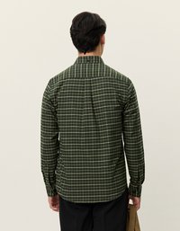 Zaļš šaha raksta krekls ar garām piedurknēm, ar apkakli un aizmugurējo satvērēju. Raksts sastāv no baltiem tīkla līnijām uz tumši zaļa fona.