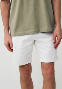 Hvide bomulds shorts med en glat tekstur, der har en afslappet pasform og en opsmøg, sammen med en kortærmet olivengrøn t-shirt.
