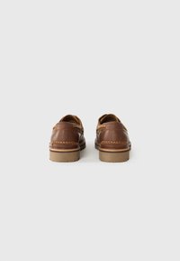 Chaussures en cuir marron avec une texture douce, présentant des coutures contrastantes en tan, un design arrondi et une semelle en caoutchouc basse.