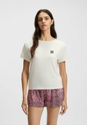 Elfenbensfärgad t-shirt med kort ärm och en liten svart logotyp, tillsammans med rosa shorts med ett svart leopardmönster. Slät textur, avslappnad stil.