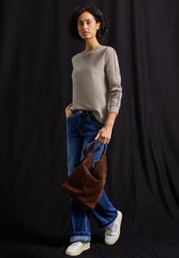 Lichtbeige trui met lange mouwen, gecombineerd met blauwe denim jeans. Een bruine suède handtas en witte sneakers maken de outfit compleet.