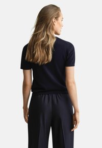 Navy korte mouwen gebreid bovenstuk met een aansluitende pasvorm, gladde textuur en ribbelkraag, gecombineerd met losse donkere broeken.