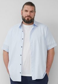 Korte mouwen lichtblauw overhemd met een gemêleerd patroon, voorzien van donkere knopen en een wit T-shirt eronder.