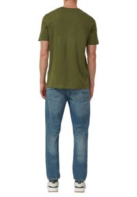 Olivengroen katoenen T-shirt met korte mouwen, gecombineerd met lichtblauwe verwassen spijkerbroek. De outfit wordt compleet gemaakt met witte sneakers.