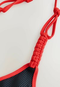 Röd bikinibehå med band som har en flätad design, som kontrasterar med ett ribbat mörkt tyg. Slät textur med knutdetaljer för en säker passform.