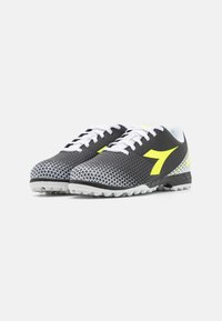 Scarpe da atletica in bianco e nero con tomaia in rete, dettagli gialli e suola testurizzata progettata per fornire trazione. Presentano lacci e un motivo triangolare.