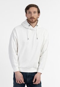 Felpa bianca con cappuccio e cordini, polsini e fondo a coste, vestibilità ampia, realizzata in tessuto morbido, abbinata a jeans scuri.