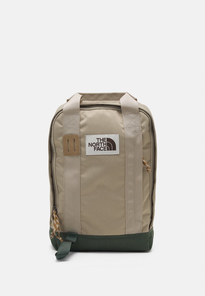 Beige kangaskangasreppu, jossa on kaksi yläkahvaa, vihreä pohja, etupuolella logopläkki ja raidallinen vetoketjun vetolaite. Ominaisuuksiin kuuluu kestävä tikkaus ja tekstuuri.