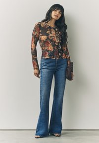 Dlhý rukáv kvetinový top s tmavým pozadím, so priliehavým strihom. Rozšírené riflové nohavice v strednom umytí. Doplnené textúrovanou kabelkou.