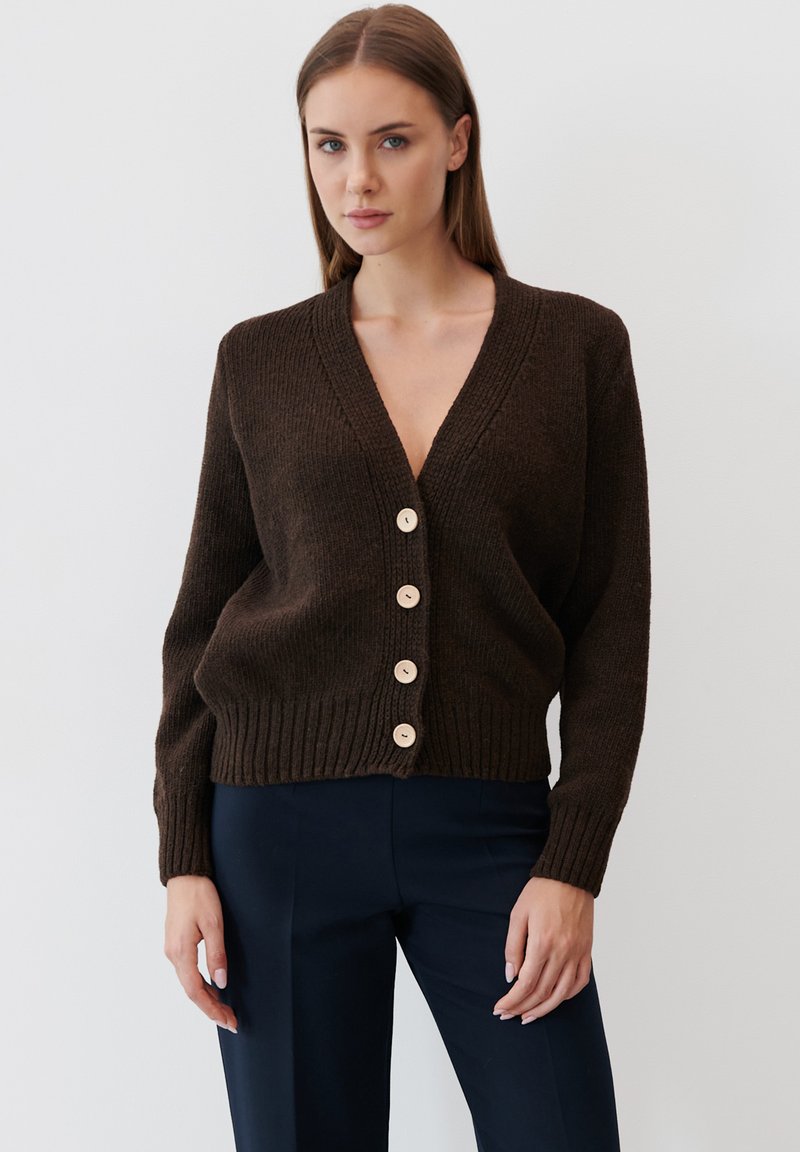 Brązowy sweter z dzianiny z głębokim dekoltem w kształcie V, prążkowanym dołem i pięcioma kremowymi guzikami z przodu. Miękka tekstura, lekko skrócony krój.