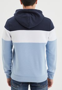 Sudadera con capucha que presenta un diseño en bloques de color con secciones en azul marino, blanco y azul claro. Confeccionada en una tela suave, con puños y dobladillo acanalados.