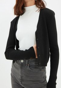 Czarny kardigan z prążkowanej tkaniny, zapinany na guziki, noszony na biały prążkowany top. W połączeniu z szarymi dżinsami o wysokim stanem. Prosty design i faktura.
