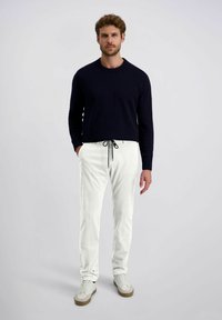 Mannen navy gebreide trui, witte drawstring broek en witte sneakers. De broek heeft een geribbelde textuur, terwijl de trui een ronde hals heeft.
