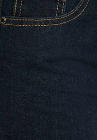 Tessuto di denim blu scuro con una sottile texture e cuciture arancioni lungo le cuciture, con un pulsante metallico visibile.