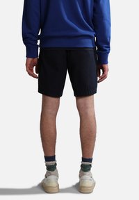 Shorts blu navy con una vestibilità rilassata, abbinati a sneaker bianche e calze a righe verdi e beige, vista da dietro.