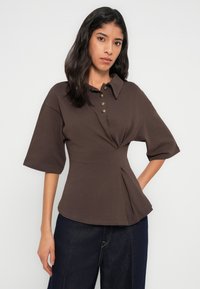Polo marron à manches courtes avec patte de boutonnage, taille cintrée avec plis et coupe décontractée. Texture de tissu lisse.