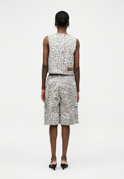 Γυναίκα που φοράει γκρι λεοπάρ αμάνικο τοπ με κουμπιά και ταιριαστά cargo σορτς μέχρι το γόνατο, με μαύρα σανδάλια με τακούνι, φαίνεται από πίσω.