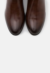 Bottines en cuir marron à finition lisse, bouts arrondis et léger éclat. Semelles en caoutchouc noir offrant adhérence et durabilité.