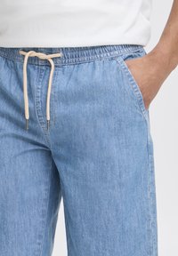 Shorts in denim azzurro chiaro con vita elasticizzata e coulisse beige. Presentano tasche laterali e un design a gamba dritta.