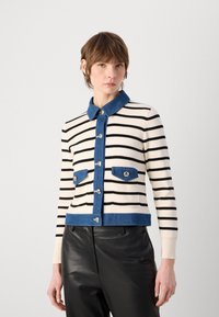 Cardigan a maglia a righe in crema e nero, con un collo in denim scuro, chiusura con bottoni e due tasche frontali con bottoni lucidi.